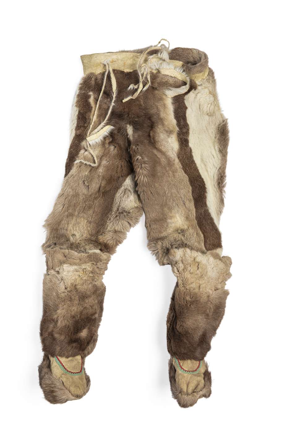 Pantalon en fourrure brune, vu de face, avec des bottes cousues à chaque jambe. Le pantalon présente des bandes verticales de fourrure brune et blanche, et des cordons pendent de la taille en cuir retourné. Les bottes, ornées de rubans verts et rouges, sont dotées d’une semelle en fourrure.