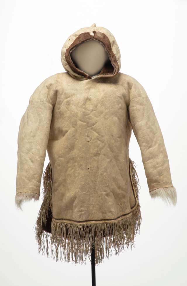 Veste en cuir beige vue de face, avec un capuchon pointu et relevé. La veste est fendue sur les côtés, et décorée de longues franges au bas et de fourrure blanche au niveau des poignets.