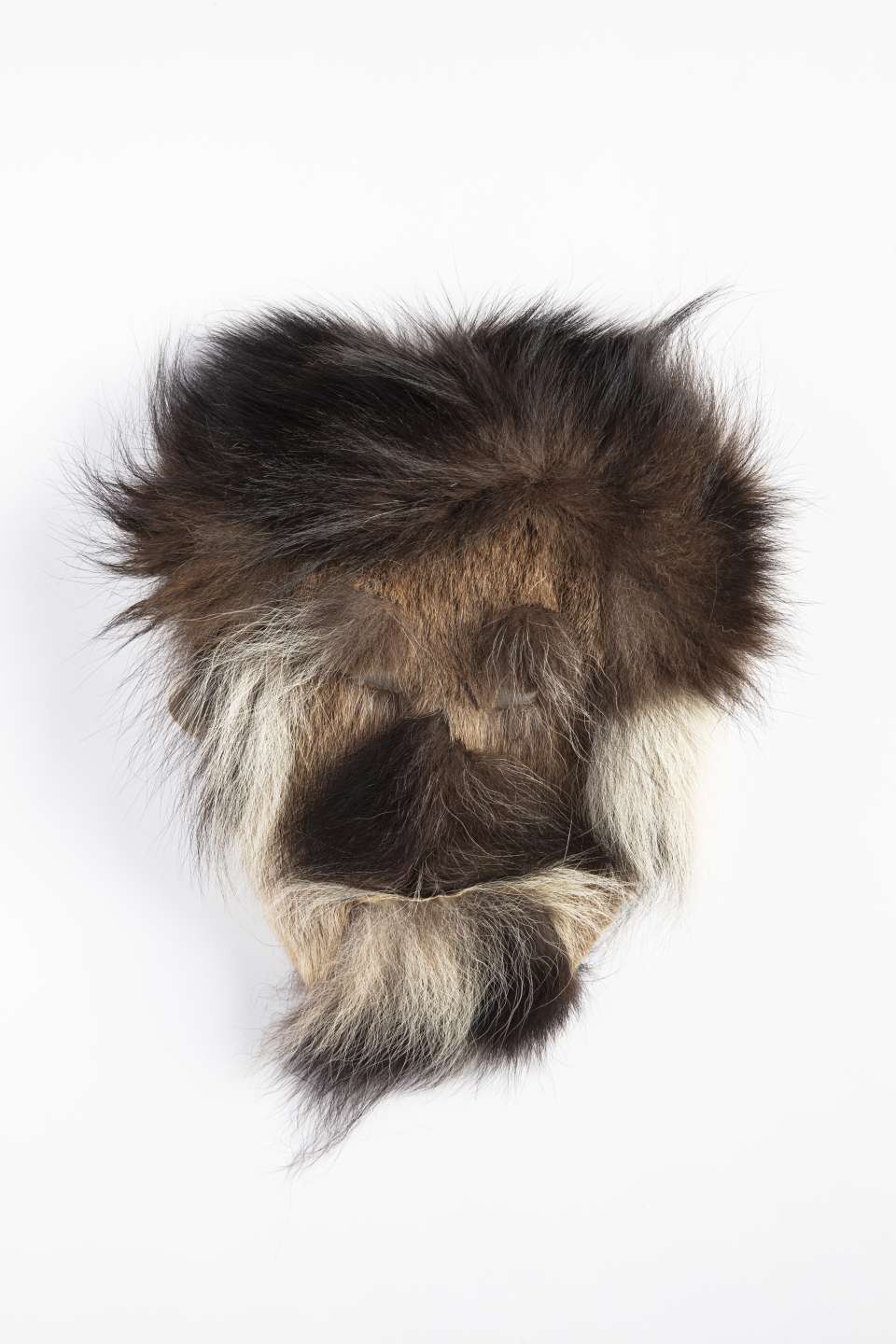 Brown fur mask, seen from the front. The fur is dark with tufts of black and brown here and there, and lighter areas under the chin and around the cheeks. The fur shows a pattern of distinct lines, creating an impression of head hair, a beard, and a moustache.