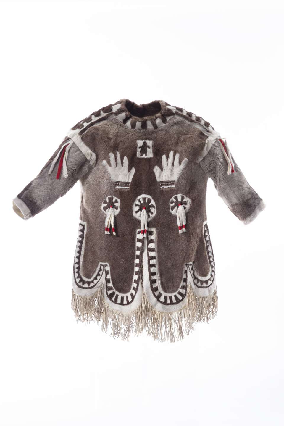 Manteau en fourrure brun ornée de motifs blancs, vu en 360 degrés. Sur la poitrine, deux mains blanches sont représentées sous un petit carré central contenant une silhouette noire. Des motifs circulaires agrémentés de lanière de fourrure et de tissu aux couleurs blanche et rouge sont visibles à l’avant et à l’arrière du manteau. Le dos présente également des motifs linéaires blancs. Le bas du manteau, le col et les épaules présentent des bandes de fourrure brune et blanche alternées. Le bas du manteau est bordé de longues franges.